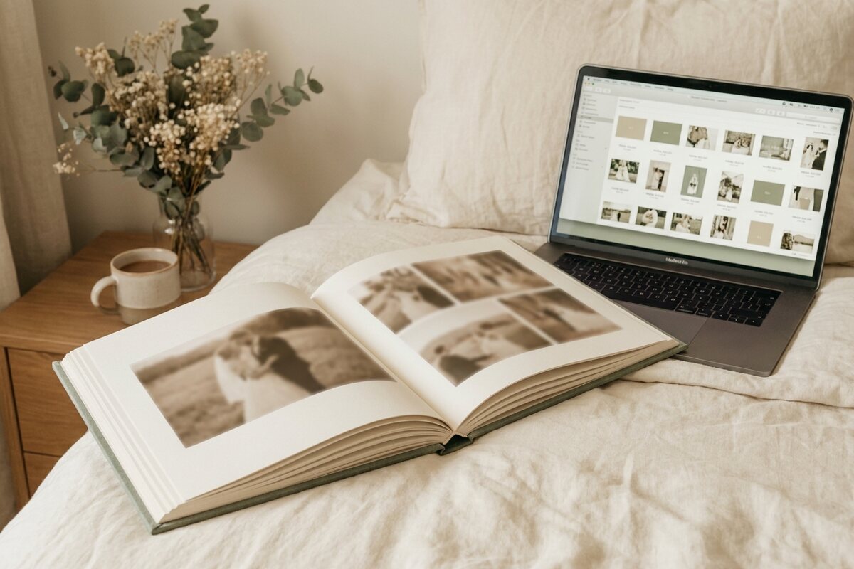 An open printed wedding photobook beside a laptop showing an organised gallery of wedding photos