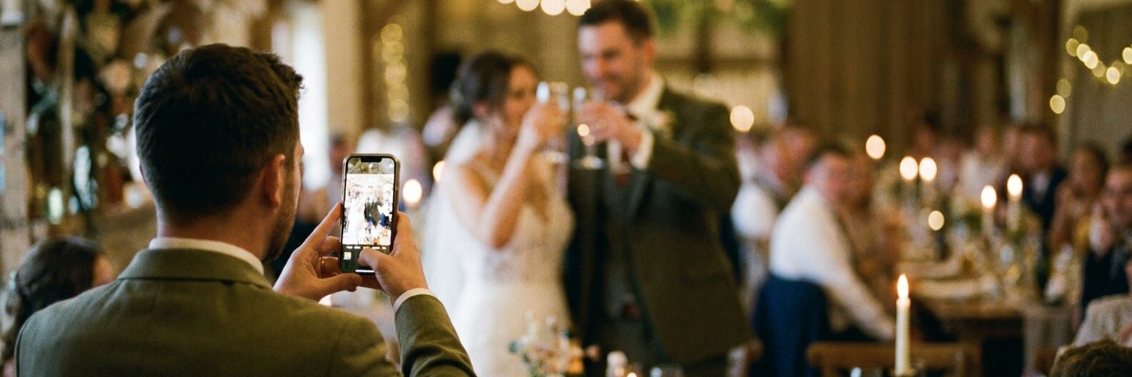 A wedding guest photographing the couple toasting during a reception