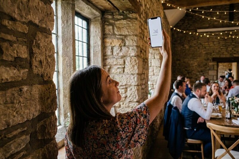 An impatient wedding guest in an old stone venue holding her phone up by the window, its screen showing no signal