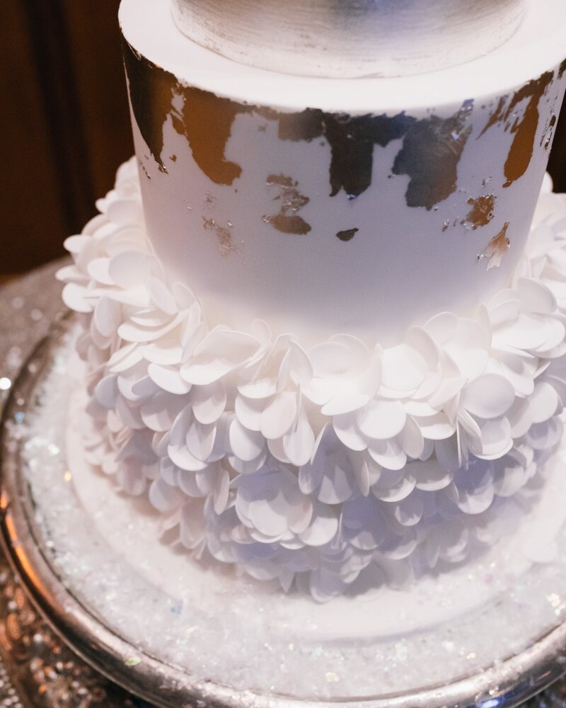 Close-up of the wedding cake's silver leaf and the layered white sugar petals on its bottom tier
