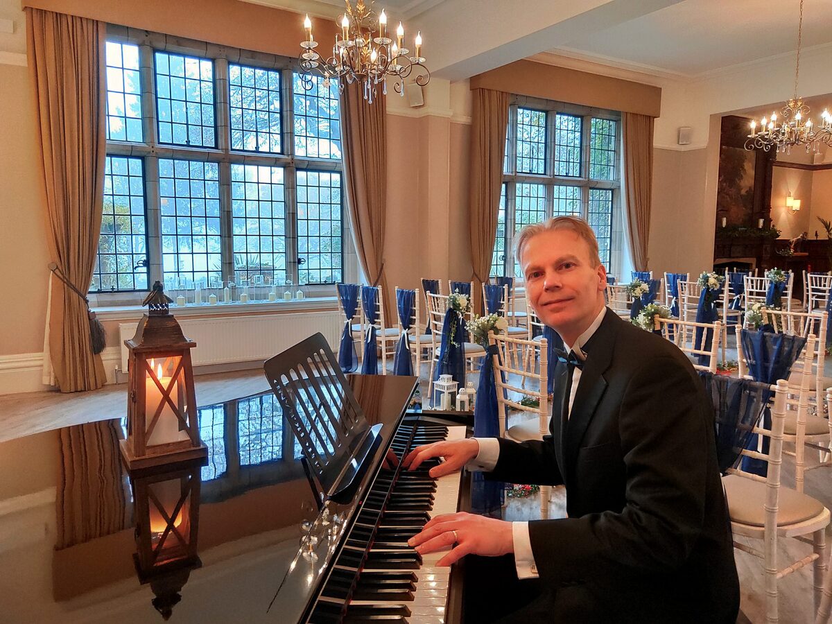 Pianist Chris Langdown in a dinner suit playing a white baby grand piano in a wedding reception room