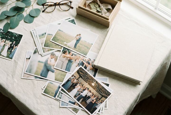 Printed wedding photographs spread on a linen tablecloth beside a linen-bound photo album and a keepsake box