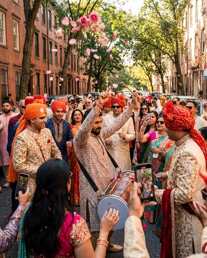 A dhol drummer leading a baraat procession while relatives record it on their phones