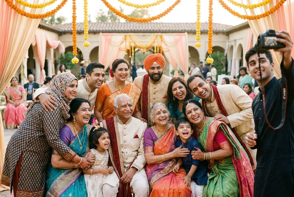 Three generations of a South Asian family laughing together for a group photo at a wedding